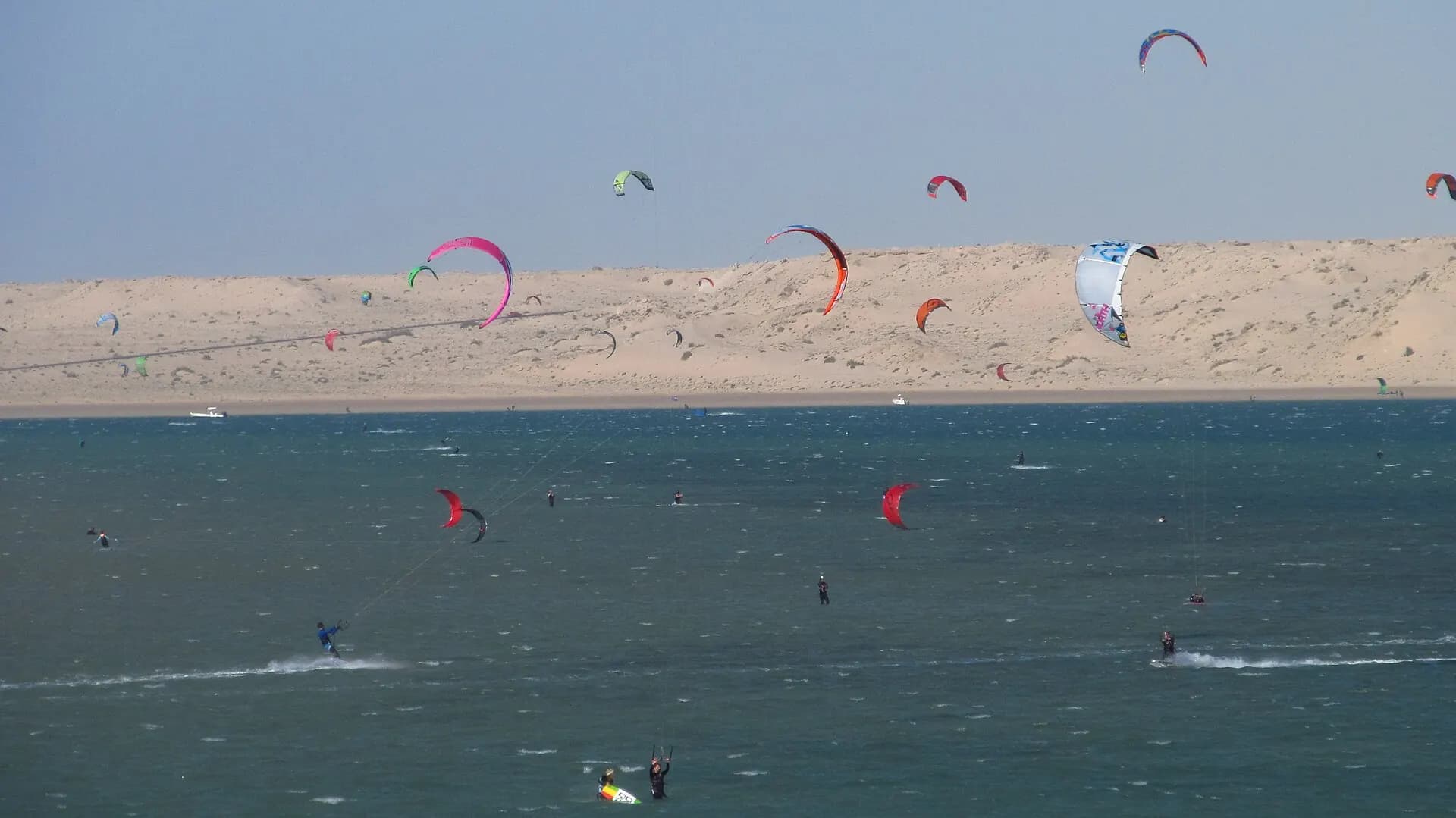 Des dizaines de kitesurfeurs sur la lagune de Dakhla, dunes en arrière-plan